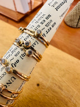 Load image into Gallery viewer, 14 karat gold fill dew drop stackable rings of a twist of vintage dictionary paper with a background of golden wood
