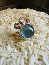 Load image into Gallery viewer, Flourite and Moonstone Statement Ring with Cubic Zirconia Accents, Handcrafted in 14k Gold Fill and Sterling Silver. Ring sitting in a bed of rice in a tarnished, vintage Silver Cup
