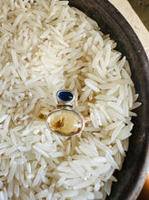 Load image into Gallery viewer, Oval Citrine Cabochon Ring with Blue Sapphire and Silver Accents. Organic hammered statement ring set with 14k Gold Fill Band. Ring displayed in a vintage silver bowl of white rice.
