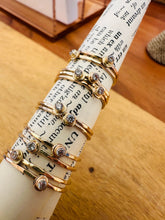 Load image into Gallery viewer, 14 karat gold fill dew drop stackable rings of a twist of vintage dictionary paper with a background of golden wood
