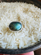 Load image into Gallery viewer, Incredible flashy blue Labradorite Statement ring.  A chunky Silver bezel encircles oval blue Labradorite on a hammered 14k Gold Fill Band. Ring is shown, held by the artist, in a vintage silver dish full of rice.
