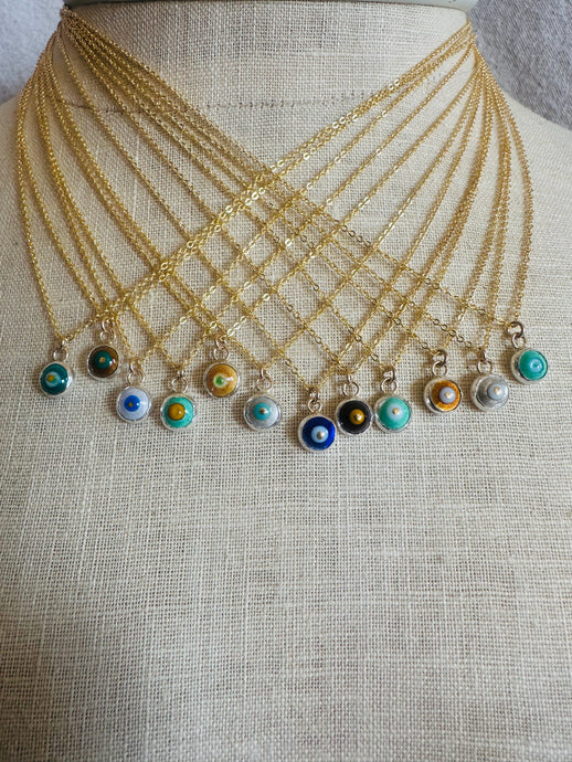 Set of gold necklaces with small, round evil eye charms on a natural linen mannequin bust.