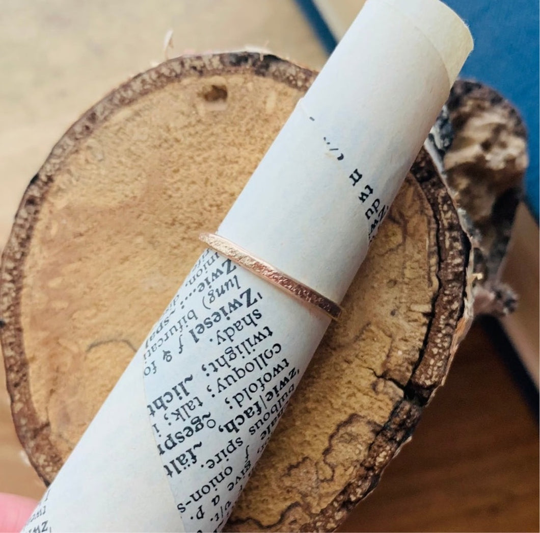 14k Gold Fill Country Roads Band Ring Shown on cone of vintage dictionary paper on round of paper birch wood.